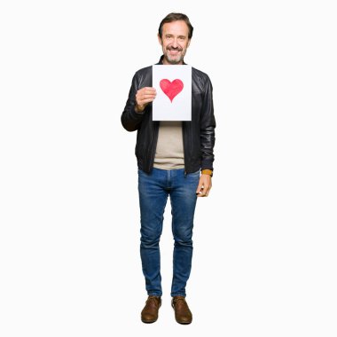 Ayakta ve diş gösterilen kendine güvenen bir gülümsemeyle gülümseyerek mutlu bir yüz ile kırmızı kalp ile kağıt tutan yakışıklı orta yaş erkek