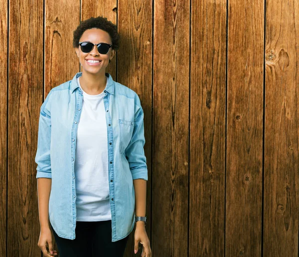 Güzel genç Afro-Amerikan kadın yüzünde mutlu ve güzel bir gülümseme ile izole arka plan üzerinde güneş gözlüğü takıyor. Şanslı kişi.