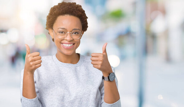 Young beautiful african american woman wearing glasses over isolated background success sign doing positive gesture with hand, thumbs up smiling and happy. Looking at the camera with cheerful expression, winner gesture.