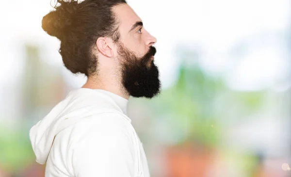 Young man with long hair and beard wearing sporty sweatshirt looking to side, relax profile pose with natural face with confident smile.