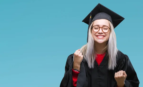 年轻的金发碧眼的女人穿着毕业生制服在孤立的背景非常高兴和兴奋做优胜者手势举起双臂 面带微笑 尖叫着要成功 庆祝理念 — 图库照片