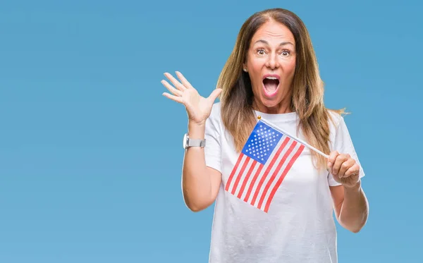 Middle age hispanic woman holding flag of United States of America over isolated background very happy and excited, winner expression celebrating victory screaming with big smile and raised hands