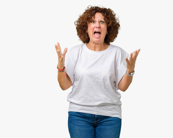 Beautiful middle ager senior woman wearing white t-shirt over isolated background crazy and mad shouting and yelling with aggressive expression and arms raised. Frustration concept.