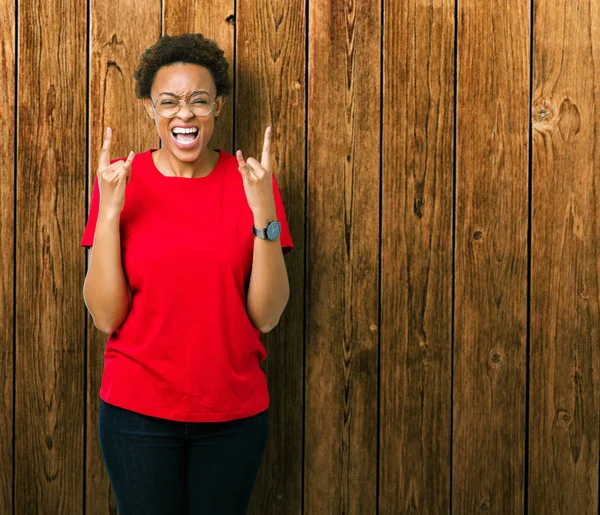 Deli ifade rock simge elle yapıyor ile bağırarak izole arka plan üzerinde gözlük güzel genç Afro-Amerikan kadın. Müzik yıldızı. Ağır kavramı.