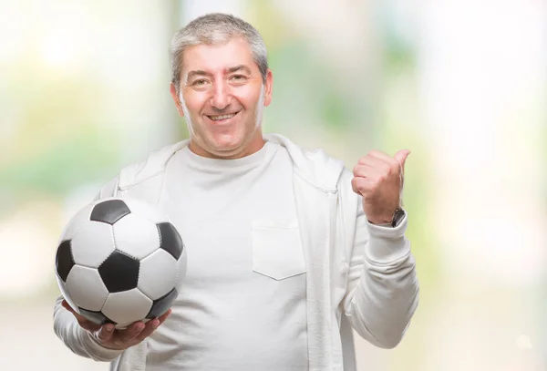指していると幸せそうな顔を笑顔で側まで親指で示す分離の背景にサッカー サッカー ボールを保持しているハンサムな年配の男性 — ストック写真