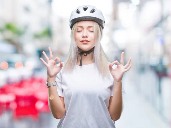 若いブロンドの女性の身に着けているサイクリスト セキュリティ ヘルメット孤立の背景の上を緩めて指で瞑想ジェスチャーをやって閉じた目を浮かべてします ヨガの概念 — ストック写真