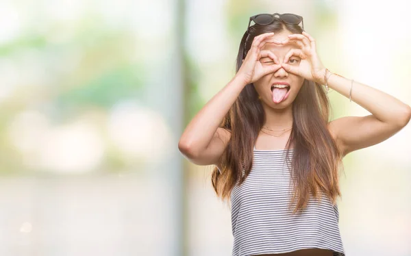 年轻的亚洲妇女戴着太阳镜在孤立的背景做确定的手势 如双筒望远镜伸出舌头 眼睛通过手指看 疯狂的表达 — 图库照片