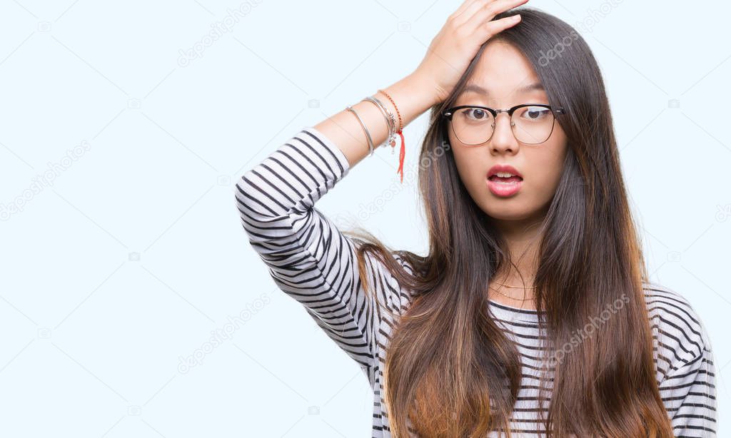 Young asian woman wearing glasses over isolated background surprised with hand on head for mistake, remember error. Forgot, bad memory concept.