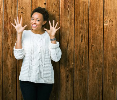 Güzel genç Afro-Amerikan kadın giyiyor kazak gösterilen ve parmakları ile işaret izole arka plan üzerinde kendinden emin ve mutlu gülümseyerek süre on numara.