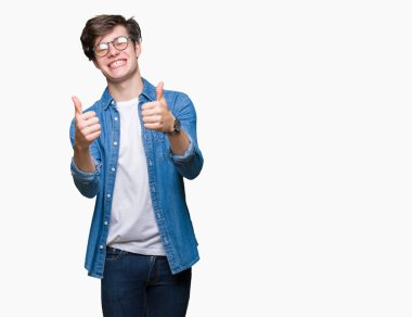 El ile pozitif jest yapıyor onaylama izole arka plan üzerinde gözlük takan genç yakışıklı adam başparmak gülümseyen ve başarı için mutlu. Kamera, kazanan jest arıyorsunuz.