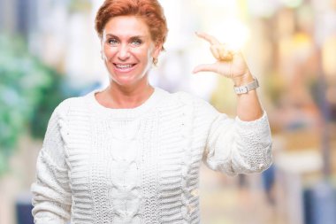 İzole arka plan gülümseyen ve boyutu işaret parmaklı ararken ve kamera işi el ile kendinden emin eller üzerinde kış kazak giyen Atrractive üst düzey beyaz Kızıl saçlı kadın. Ölçü kavramı.