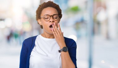 Genç güzel Afrikalı-Amerikalı kadın izole arka plan üzerinde gözlük el ağzıyla kapsayan yorgun esneme sıkılmış. Restless ve uyku hali.