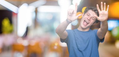 Üzerinde gösterilen ve parmakları ile işaret izole arka plan mavi t-shirt giyen genç yakışıklı adam kendinden emin ve mutlu gülümseyerek süre yedi numara.