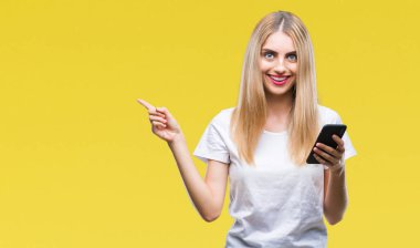 Genç güzel sarışın kadın Smartphone izole arka tarafına el ve parmak ile işaret çok mutlu üzerinde kullanma