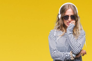 Stresli ve gergin elle çivi ısırma ağzına bakarak izole arka plan üzerinde kulaklık ve güneş gözlüğü giyen güzel genç sarışın kadın. Anksiyete sorunu.