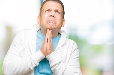 Orta yaş Arap yalvarıyor ve umut ifade yüzünde çok duygusal ve endişe ile birlikte elleriyle dua izole arka plan üzerinde sweatshirt giyen adam. Bağışlanmak. Din kavramı.