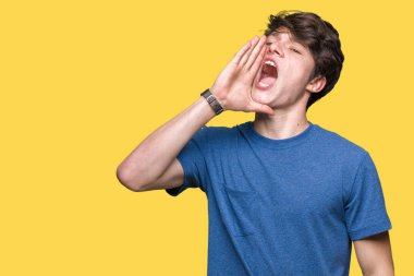 Bağırarak ve ağzı üzerinde el ile yan için çığlık izole arka plan üzerinde mavi t-shirt giyen genç yakışıklı adam. İletişim kavramı.