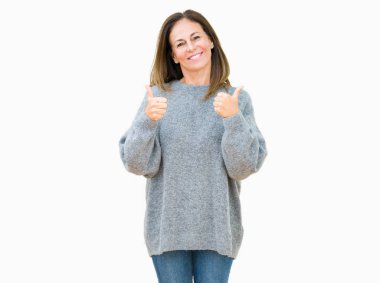 Güzel orta yaş kadın izole arka plan başarı işareti üzerinde kış kazak giyen el ile olumlu jest yapıyor, gülümseyen ve mutlu kadar başparmak. Neşeli ifade ile kamera bakarak, kazanan jest.