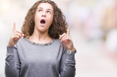 Güzel esmer kıvırcık saçlı Genç kız izole arka plan üzerinde bir kazak giyiyor hayret ve yukarıya bakıp parmakları ile işaret şaşırttı ve silah kaldırdı.