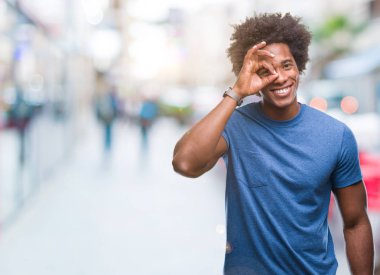 Afro Amerikalı adam gülümsüyor, parmakları ile mutlu yüz üzerinden seyir göz el ile ok jest yapıyor izole arka plan üzerinde.