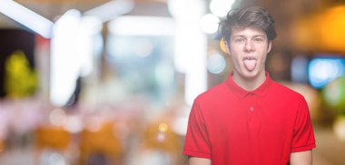 Genç yakışıklı dilini izole arka plan üzerinde kırmızı t-shirt giyen adam out komik ifade ile mutlu. Duygu kavramı.