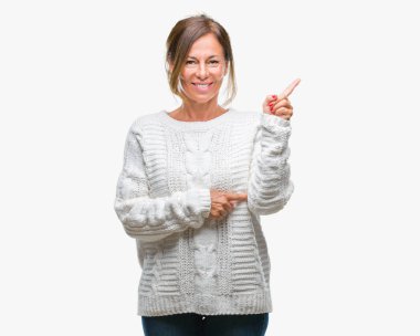 Kameraya bakarak yan el ve parmak ile işaret orta yaş üst düzey İspanyol kadın yüzünde kocaman bir gülümseme ile izole arka plan üzerinde kış kazak giyiyor.