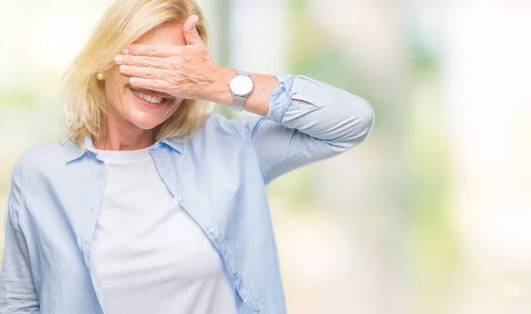 Middle age blonde woman over isolated background smiling and laughing with hand on face covering eyes for surprise. Blind concept.