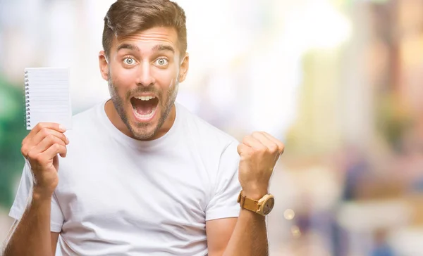 Joven Hombre Guapo Sosteniendo Cuaderno Sobre Fondo Aislado Gritando Orgulloso —  Fotos de Stock