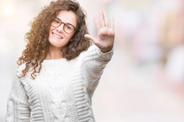 Güzel esmer kıvırcık saçlı Genç kız giyiyor kış kazak gösterilen ve parmakları ile işaret izole arka plan üzerinde beş kendinden emin ve mutlu gülümseyerek iken numara.