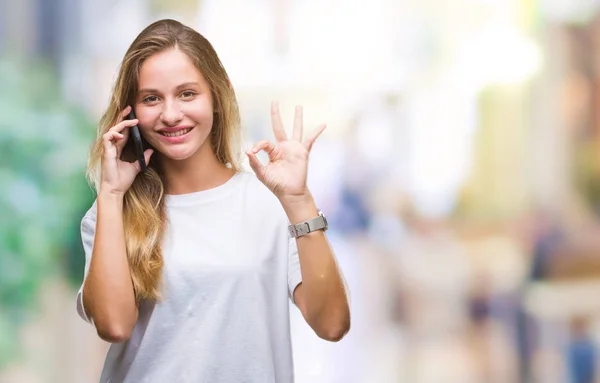 年轻美丽的金发碧眼的女人打电话使用智能手机在孤立的背景做确定的标志与手指 优秀的象征 — 图库照片