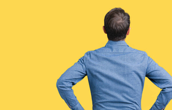 Красивый пожилой элегантный мужчина на изолированном фоне, стоящий задом наперёд и смотрящий с руками на тело.
