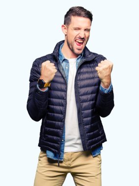 Gülümseyen ve başarı için çığlık çok mutlu ve heyecanlı kaldırdı, silah ile kazanan jest yapıyor bir kış palto giyiyor yakışıklı adam. Kutlama kavramı.