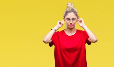 Yüksek sesle müzik gürültü rahatsız ifade parmaklarıyla kulaklarıyla kapsayan izole arka plan üzerinde kırmızı t-shirt ve gözlük giyen genç güzel sarışın kadın. Sağır kavramı.