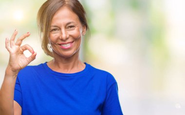 Gülümseyen izole arka plan üzerinde orta yaş İspanyol kadın kıdemli el ve parmaklar ok işaretiyle yapıyor olumlu. Başarılı ifade.