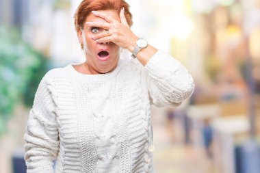 Mahcup ifadeyle parmaklarımın arasından seyir yüz ve gözler el ile kapsayan şok izole arka plan bakmak üzerinde kış kazak giyen Atrractive üst düzey beyaz Kızıl saçlı kadın.