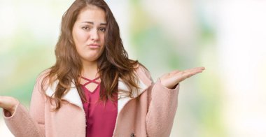 Artı boyutu genç kadın güzel üzerinde kış palto giyiyor arka plan clueless ve şaşkın bir ifadeyle kollar ve eller kaldırdı izole. Şüphe kavramı.