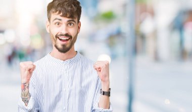 Genç yakışıklı iş adamı izole arka plan kutlama üzerinde şaşırttı ve başarı için kaldırdı kollarını açarak hayret ve gözleri açık. Kazanan kavramı.