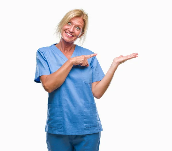 中年の金髪女性分離背景驚くし 手とを提示 指で指している間カメラに笑顔に医師看護師の制服を着て — ストック写真