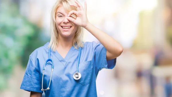 美しい金髪女医女性の笑顔 幸せそうな顔で指を通して見る目の手で のジェスチャーを行う分離の背景に医療の制服を着て — ストック写真