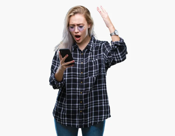 年轻的金发碧眼的女人发短信发送消息使用智能手机在孤立的背景恼火和沮丧的喊声与愤怒 疯狂和大喊大叫与提高的手 愤怒的概念 — 图库照片