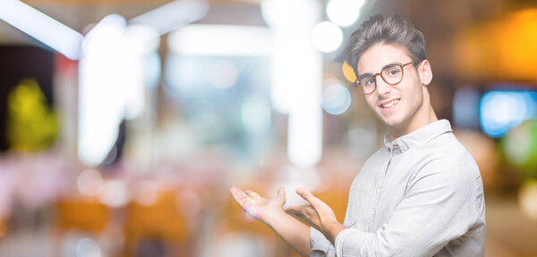 Young handsome man wearing glasses over isolated background Inviting to enter smiling natural with open hand