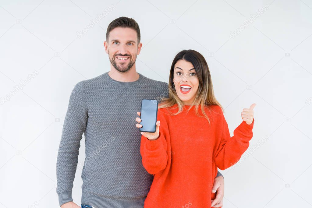 Young couple showing smartphone screen over isolated background pointing and showing with thumb up to the side with happy face smiling