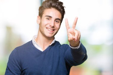 Genç yakışıklı iş adamı mutlu yüz zafer işareti yaparken kameraya göz kırpıyor ile gülümseyen izole arka plan üzerinde. İki numaralı.