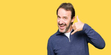 Orta yaş yakışıklı adam yapıyor gülümseyen bir kazak giyen telefon hareketi ile el ve parmak telefonda konuşuyor gibi. Kavramları iletişim.