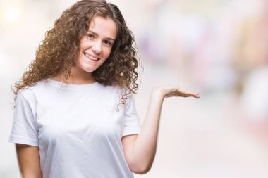 Neşeli sunulması ve kameraya bakarak avucunun ile işaret gülümseyen izole arka plan üzerinde rahat t-shirt giyen güzel esmer kıvırcık saçlı Genç kız.