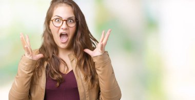 Bir elbise ve deri giyen güzel artı boyutu genç kadın deli kutluyor izole arka plan üzerinde ceket ve silah ile başarı için yükseltilmiş ve açık gözleri heyecanlı çığlık hayrete düşürdü. Kazanan kavramı