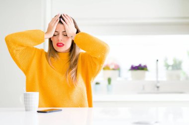 Genç güzel kadın ev umutsuz ve stresli baş ağrısı muzdarip çünkü, kahve içme ağrı ve migren. Ellerini kafasına.
