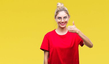 Hareketi el ile mutlu yaşasın yapıyor izole arka plan üzerinde kırmızı t-shirt ve gözlük giyen genç güzel sarışın kadın. Kameraya bakarak başarı gösteren ile ifade onaylama.