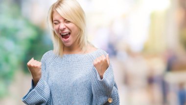 Üzerinde kış kazak giyen genç güzel sarışın kadın gülümseyerek ve başarı için çığlık arka plan çok mutlu ve heyecanlı kaldırdı, silah ile kazanan jest yapıyor izole. Kutlama kavramı.