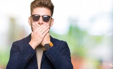 Genç yakışıklı zarif adam ağız hata için elleriyle kapsayan şok güneş gözlüğü takıyor. Gizli kavramı.